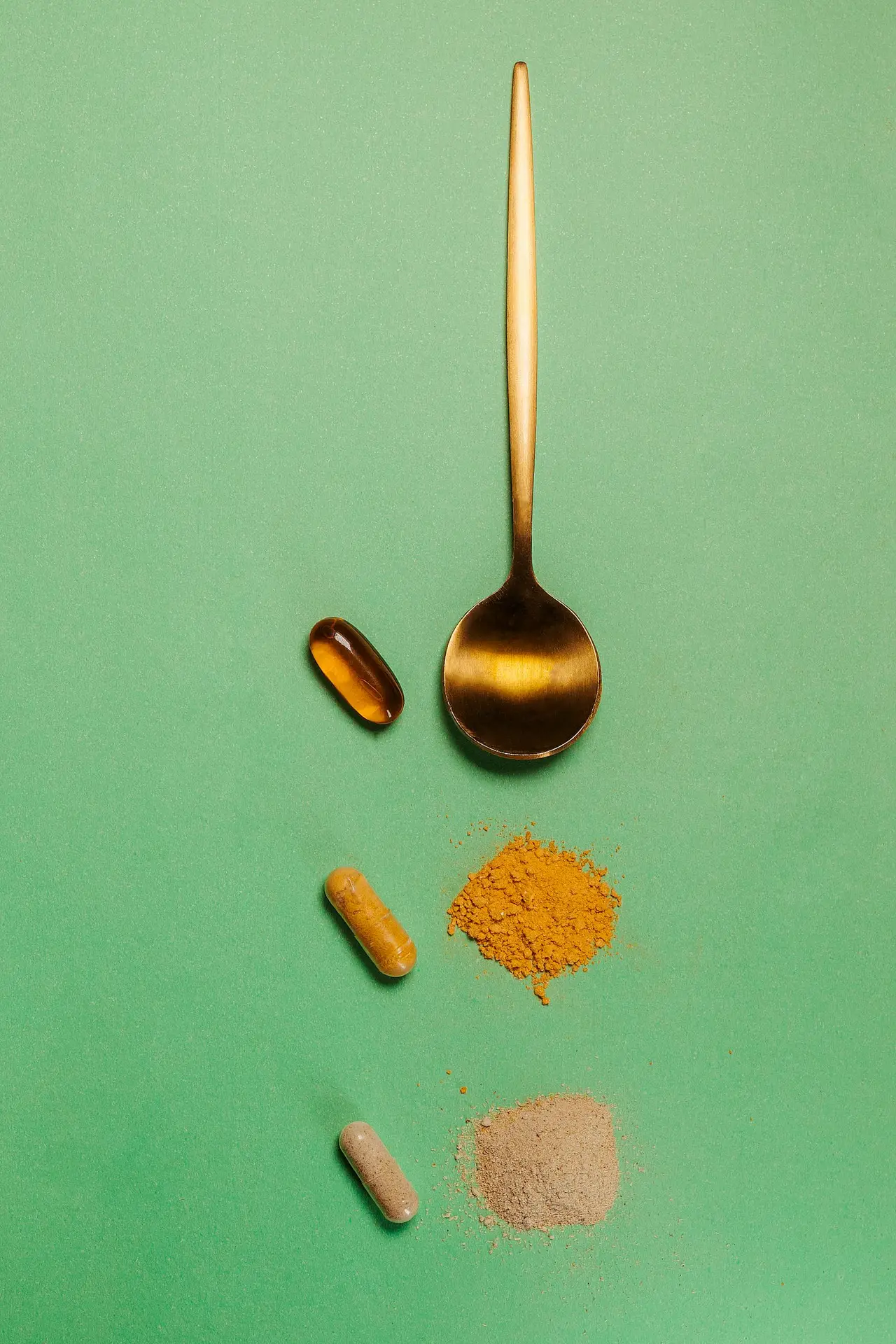 Vitamins and supplements arranged with a golden spoon on a green surface.